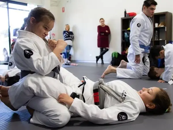 Young students practicing Brazilian Jiu Jitsu techniques at Alpha Jiu Jitsu Academy, focusing on guard positions and technique refinement during class.