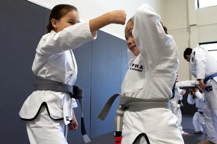 Young students practicing Brazilian Jiu Jitsu techniques during a kids' class at Alpha Jiu Jitsu Academy, focusing on form and discipline.