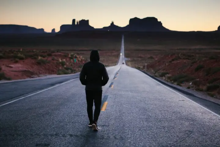 Person walking alone on an open road with a scenic desert landscape, symbolizing perseverance, journey, and personal growth.