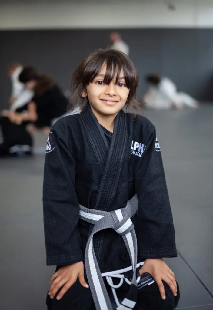 Young student wearing a black gi and gray belt at Alpha Jiu Jitsu Academy, smiling confidently during training.