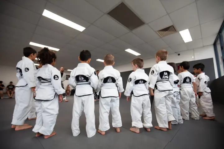 Group of children in white gis standing in formation during a Brazilian Jiu Jitsu class at Alpha Jiu Jitsu Academy, ready for instruction.