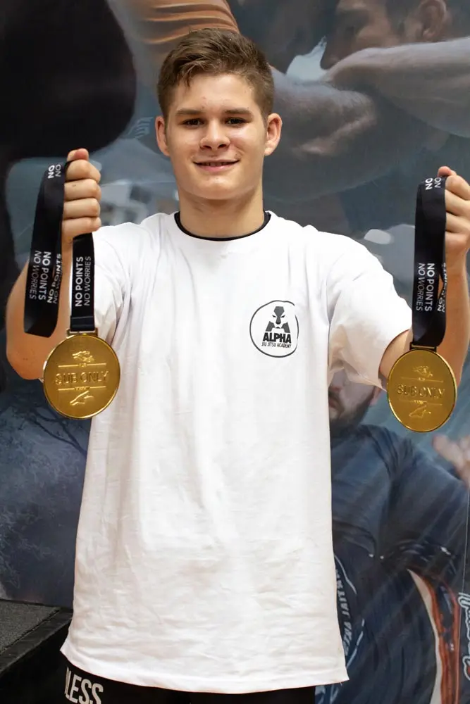 Alpha Jiu Jitsu Academy student proudly holding two gold medals after a successful competition, showcasing achievement and excellence in Brazilian Jiu Jitsu.