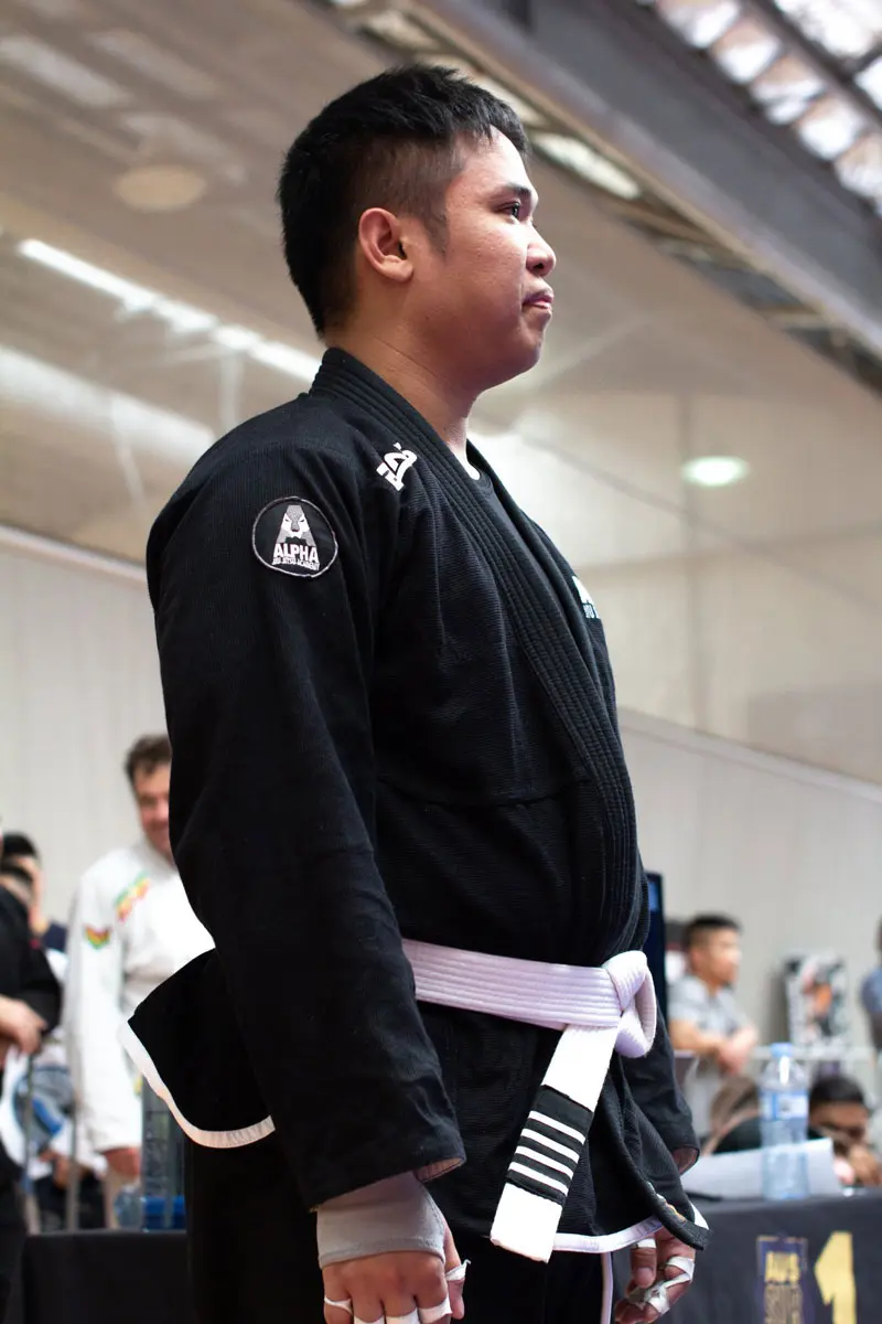 Alpha Jiu Jitsu student in a black gi with a white belt, focused and ready during a martial arts competition.